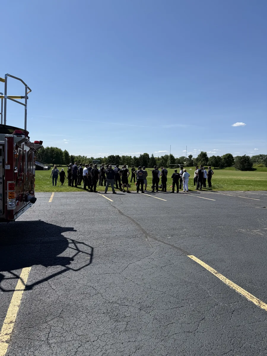 Fire, EMS, and law-enforcement personnel gather on a field for a debrief during a multi-agency drill.